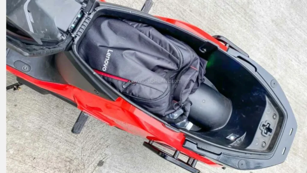 River Indie electric scooter's underseat storage (43 Litres) open, with a black backpack and helmet stored inside.