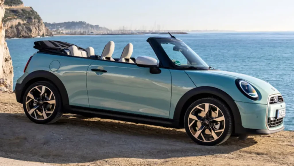 New Mini Cooper S Convertible launched side view in blue with roof down beside coastline